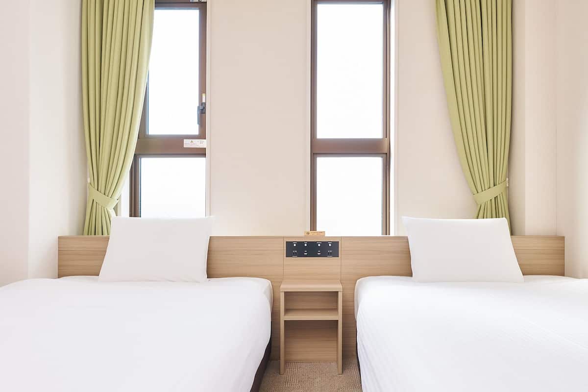 Hotellihuone, jossa on kaksi sänkyä, yöpöytä ja ikkuna, jossa on verhot.