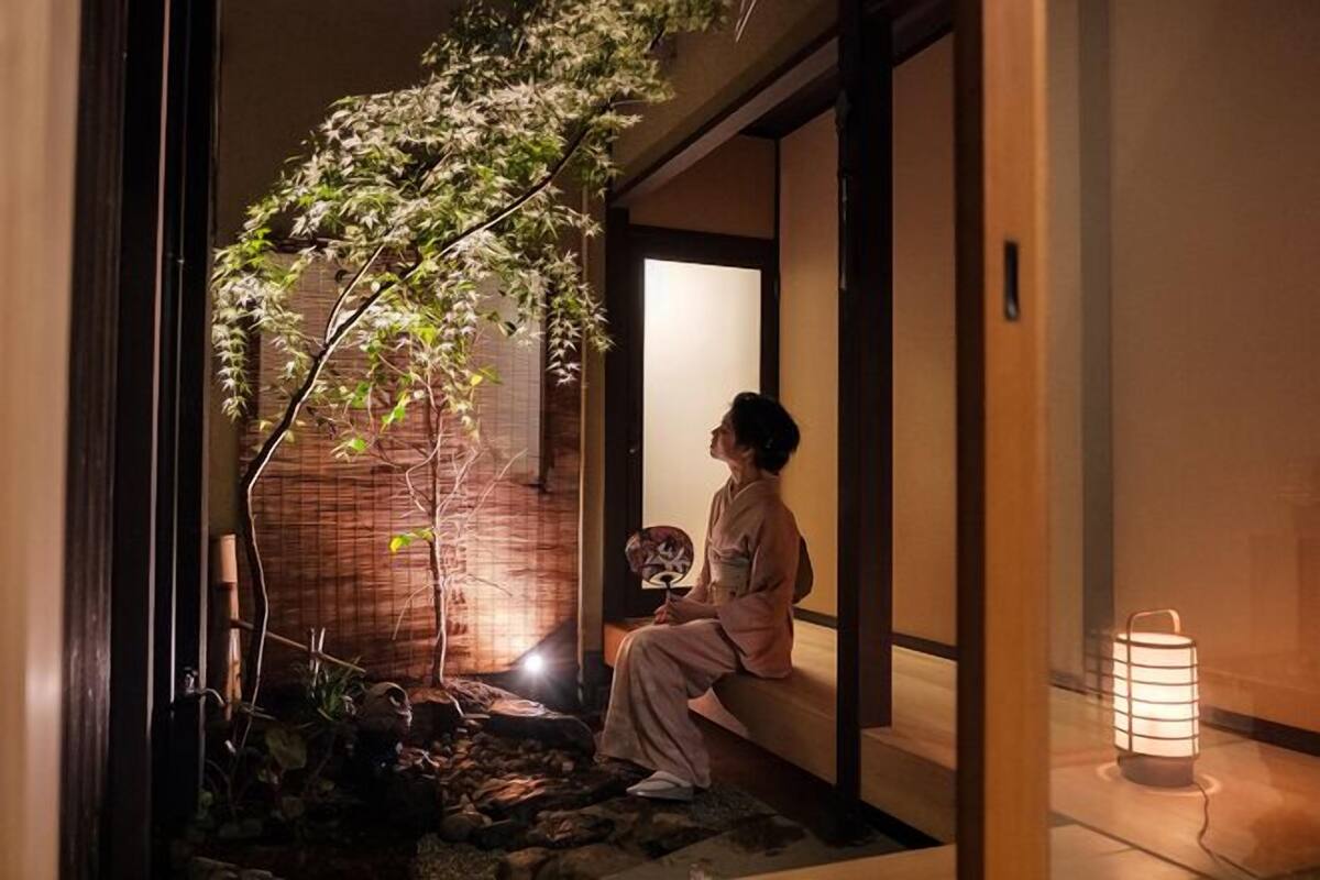 Un interior japonés tradicional con una persona sentada junto a una ventana, un farol y un bonsái.