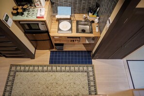 Una cocina compacta con microondas, refrigerador, pileta y un tapete azul estampado.