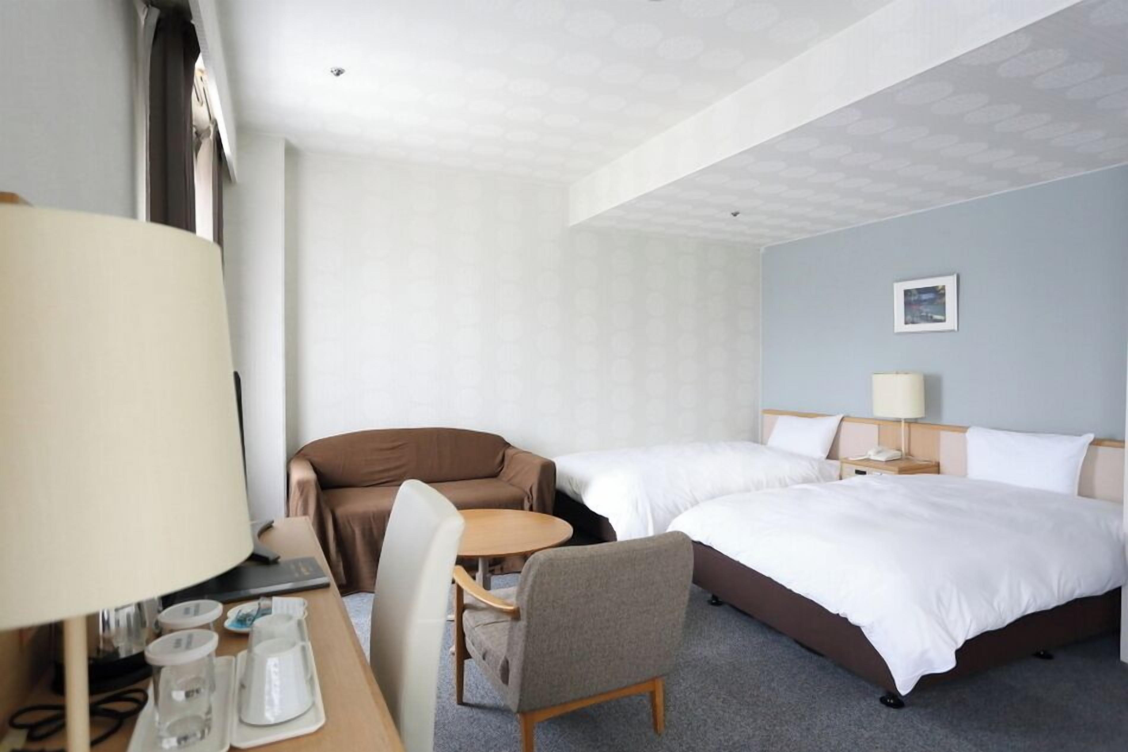 Ein Hotelzimmer mit zwei Betten, einem Schreibtisch mit Lampe, einem Stuhl und einem kleinen Tisch.
