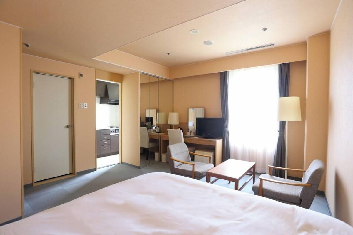 A hotel room with a bed, desk, chairs, a television, and a mirror.