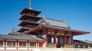 Une pagode traditionnelle à plusieurs niveaux, avec une flèche centrale imposante, entourée d’un bâtiment blanc agrémenté de touches de rouge et de cadres de fenêtres verts.