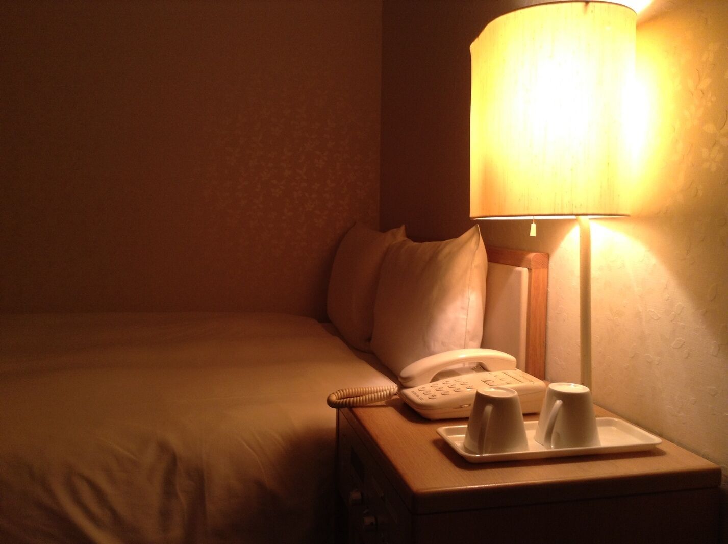 Ein Hotelzimmer mit Bett, Nachttisch mit Lampe, Telefon und Tablett mit Tassen.