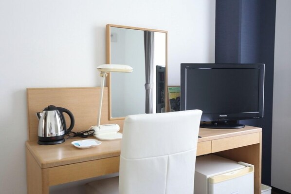 Une chambre d’hôtel avec un bureau en bois, une chaise blanche, une télévision, une bouilloire, une lampe et un miroir.