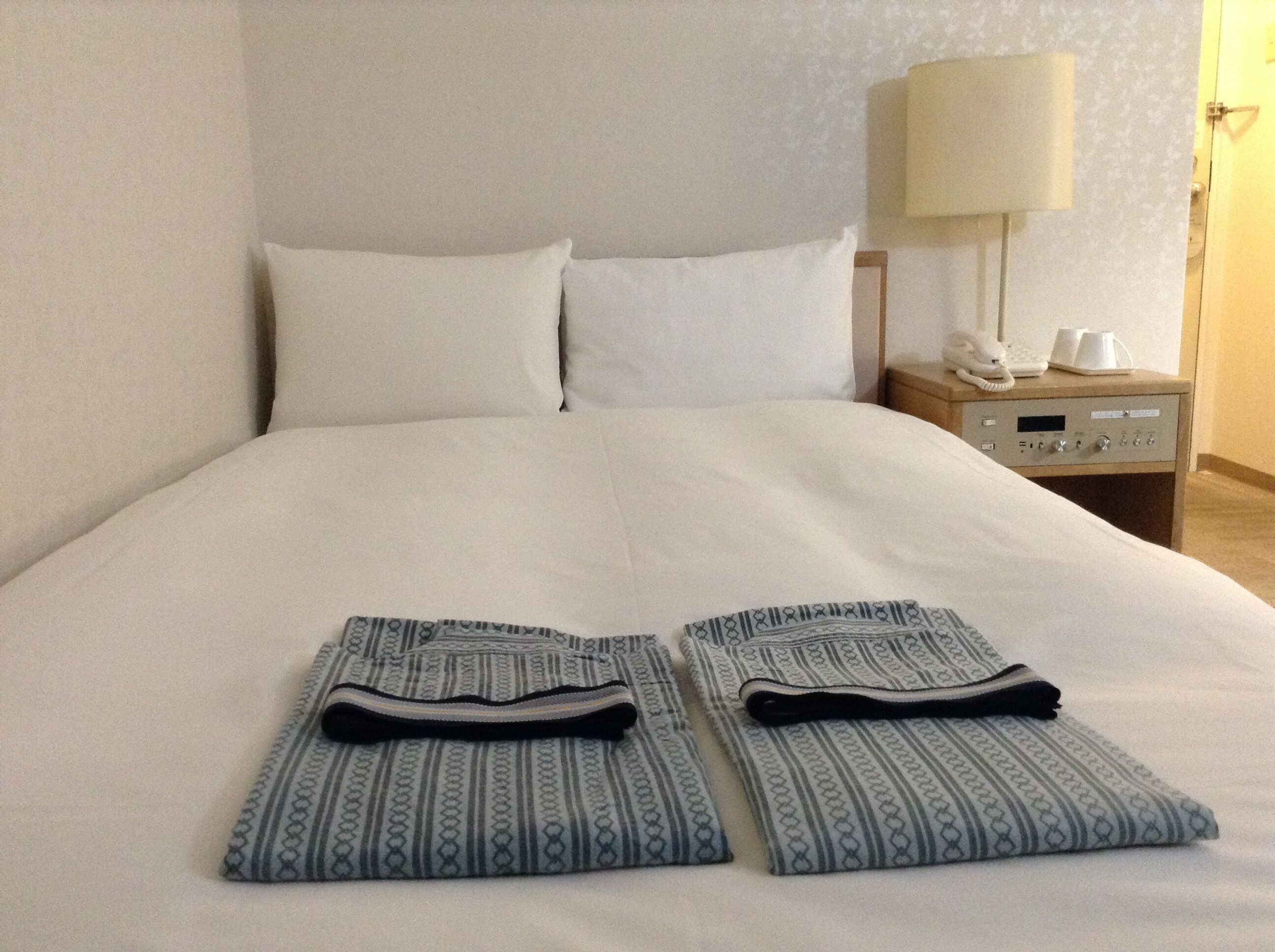 Una cama bien hecha con ropa de cama blanca, una mesita de noche con una lámpara y un teléfono.