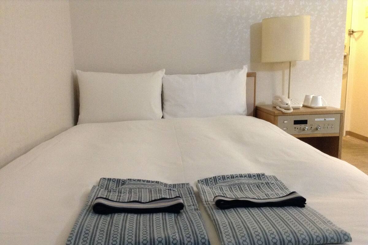A neatly made bed with white linens, a bedside table with a lamp, and a phone.