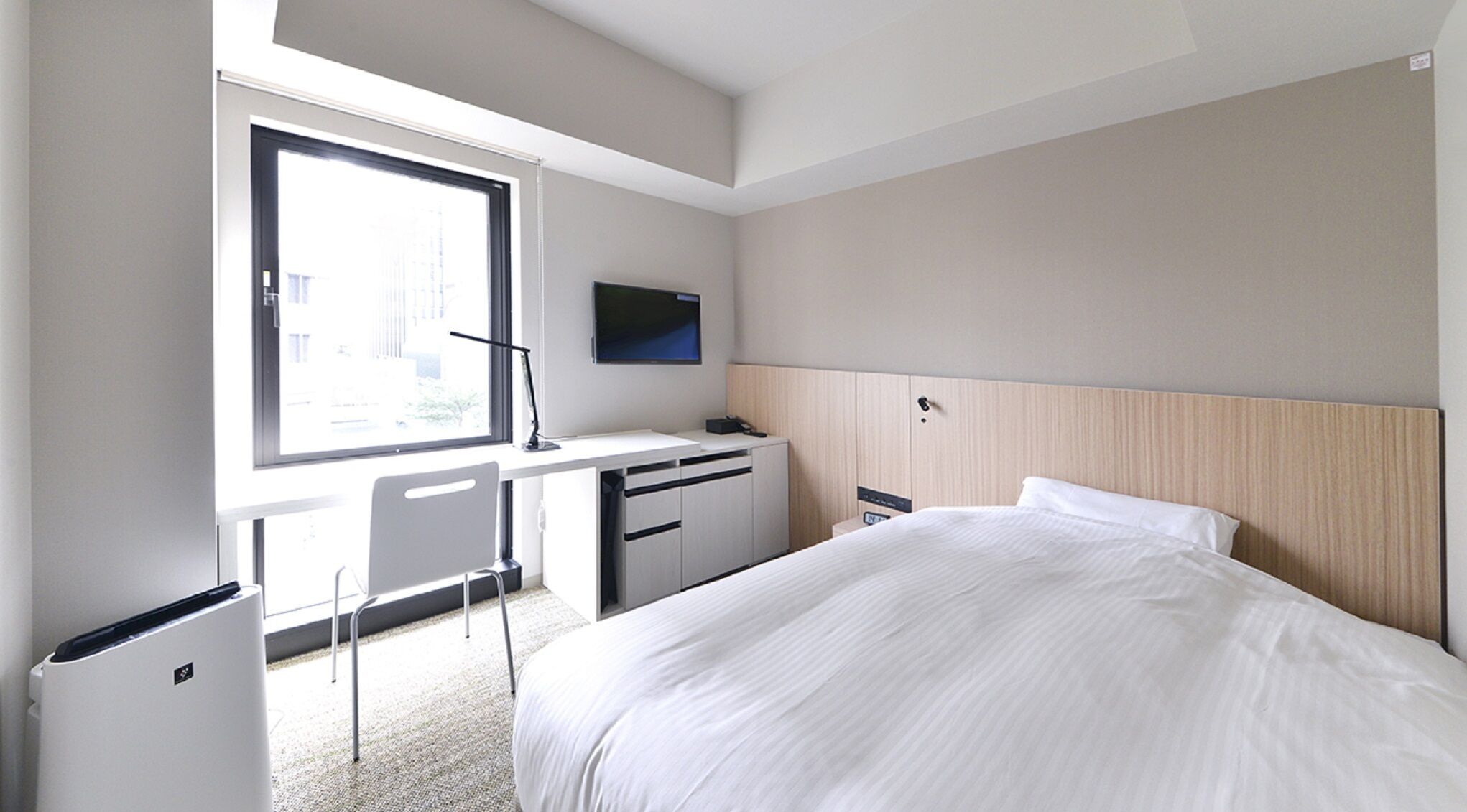 A hotel room with a bed, desk, chair, TV, and a window.