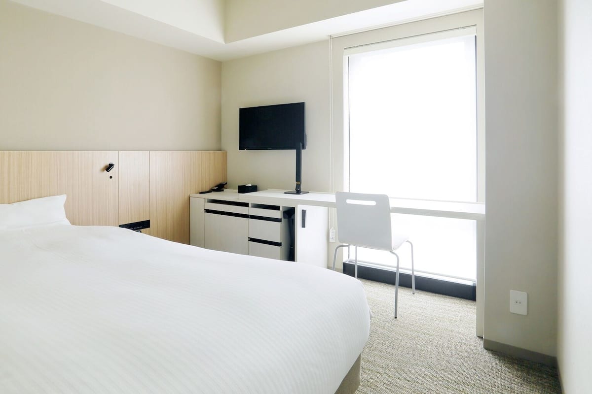 Quarto de hotel com uma cama grande, uma escrivaninha, uma cadeira, televisão de tela plana e janela.