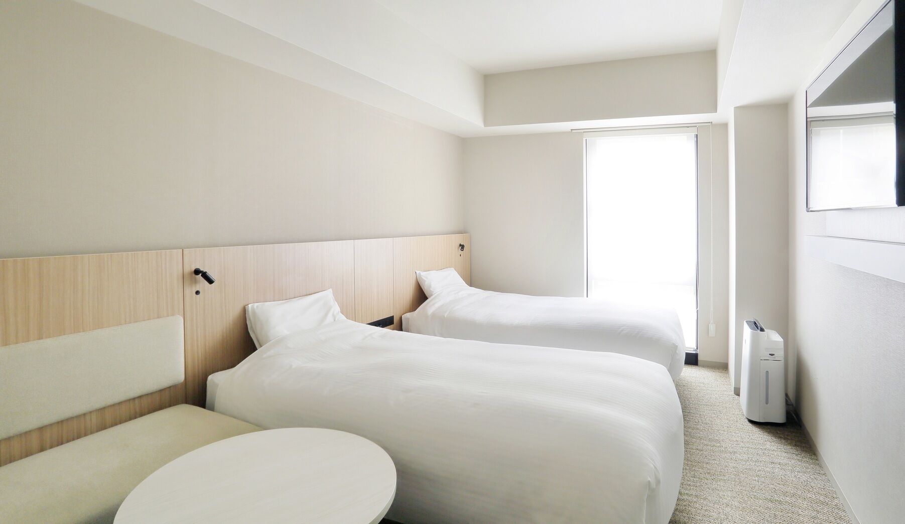 A hotel room with two beds, a round table, and a window.