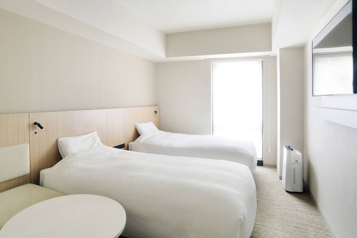 Quarto de hotel com duas camas, uma mesa redonda e uma janela.
