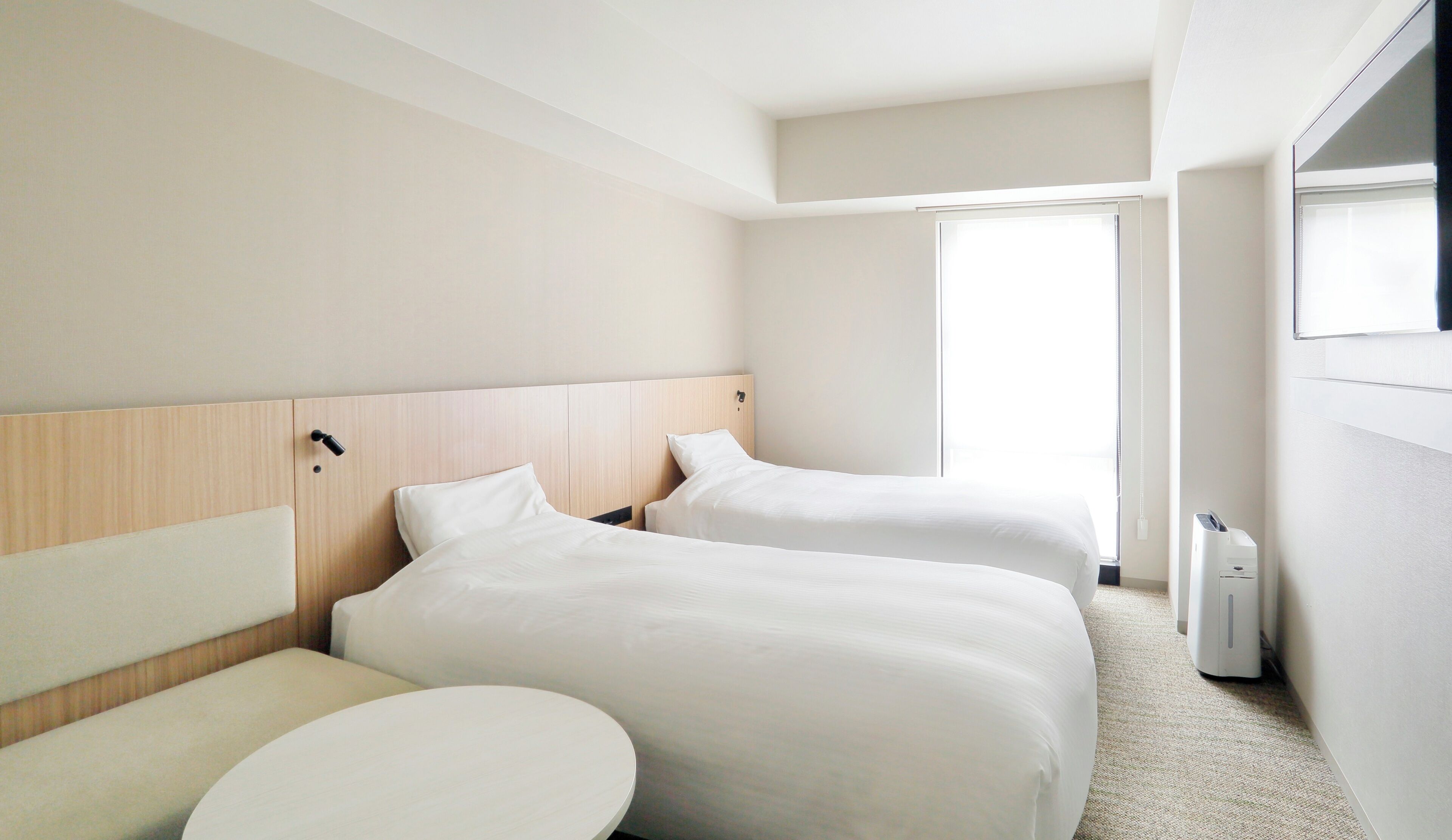 Ett hotellrum med två sängar, ett runt bord och ett stort fönster.