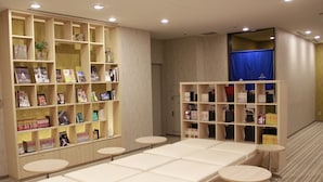 Une chambre d’hôtel avec un grand lit, un coin salon avec des tables rondes, et deux étagères remplies de livres et de magazines.
