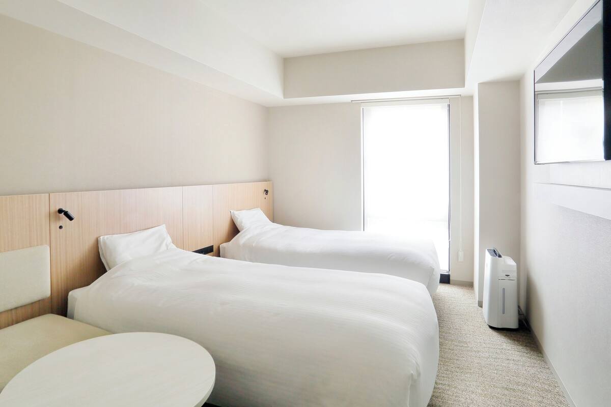 Quarto de hotel com duas camas, uma mesa redonda e uma janela grande.