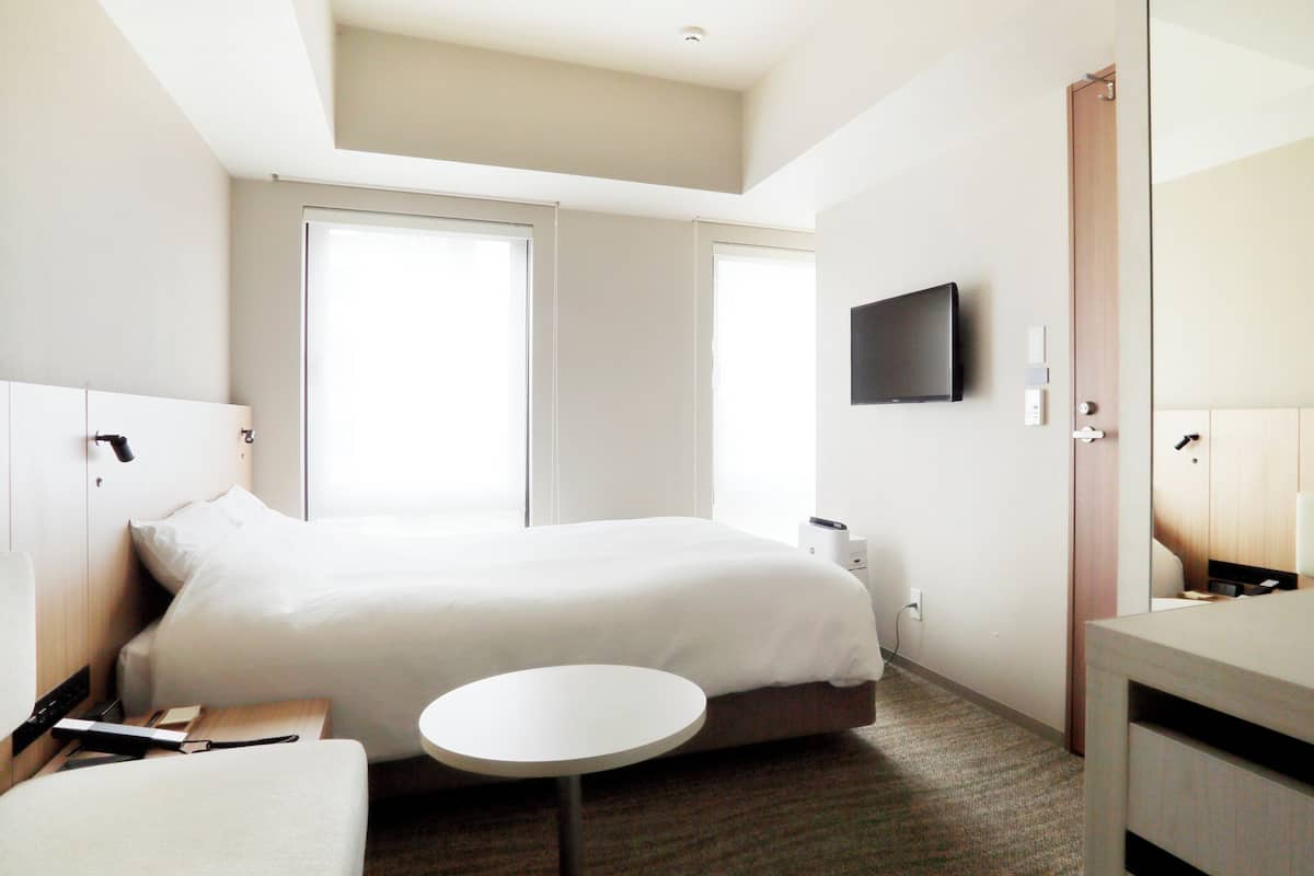 Quarto de hotel com cama, mesa de cabeceira, abajur e televisão na parede.