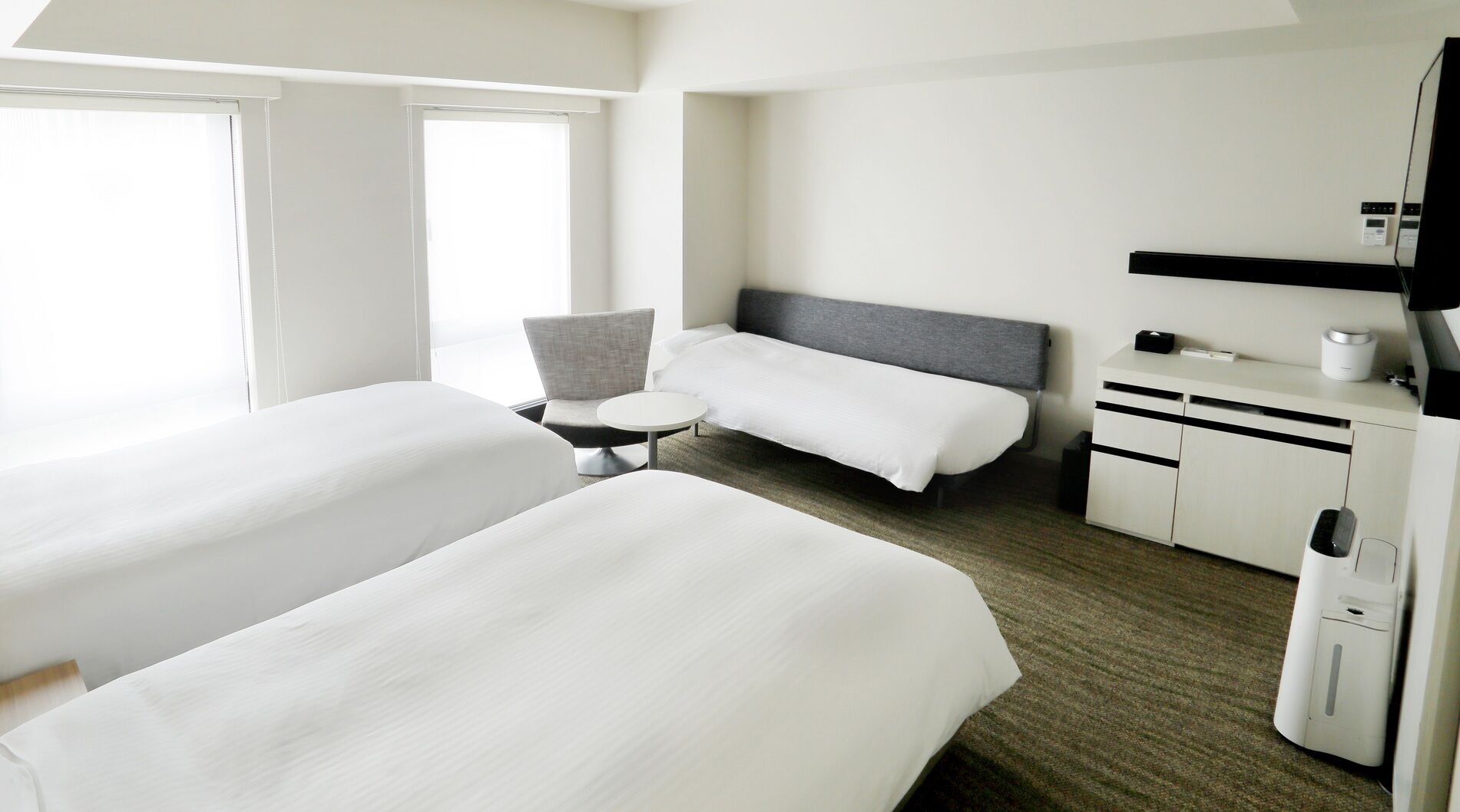 A hotel room with two beds, a small round table, a chair, a desk with a computer, and a television.
