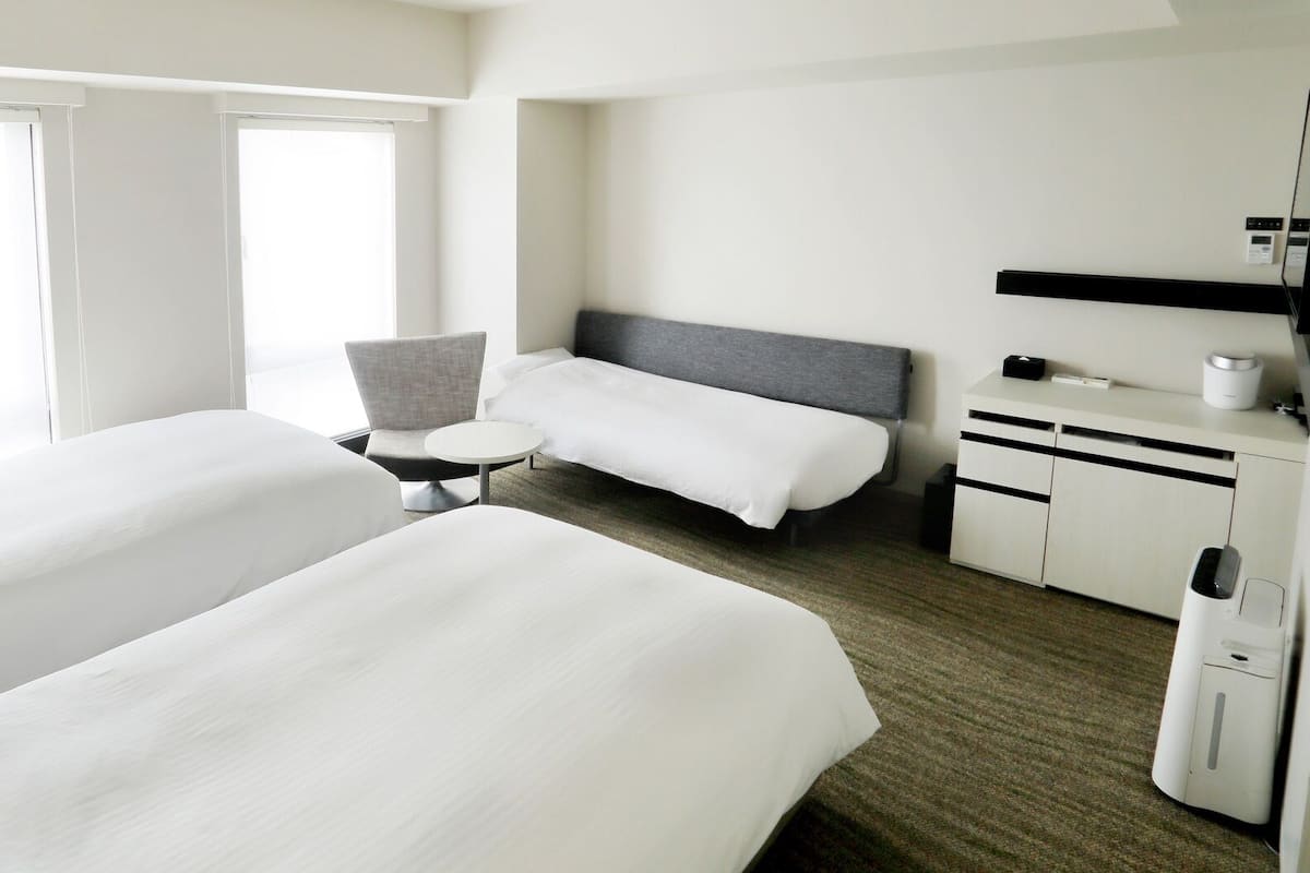 A hotel room with two beds, a small round table, a chair, a desk with a computer, and a television.