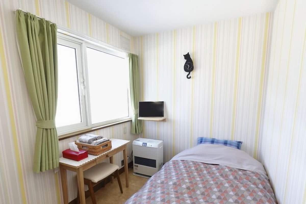 Ein Schlafzimmer mit einem Bett, einem Schreibtisch mit Stuhl, einer Waschmaschine und einem an der Wand befestigten Fernseher.