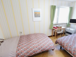 Una habitación con dos camas, un escritorio, una ventana con cortinas, un televisor montado en la pared y un radiador.