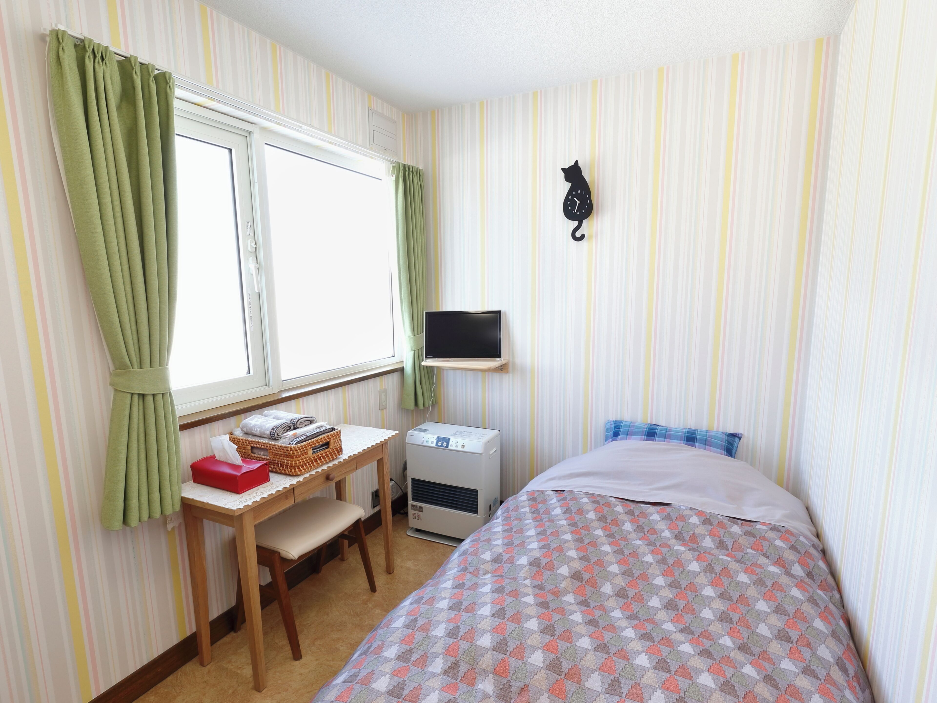 A room with a bed, a desk with a chair, a television, and a wall clock.