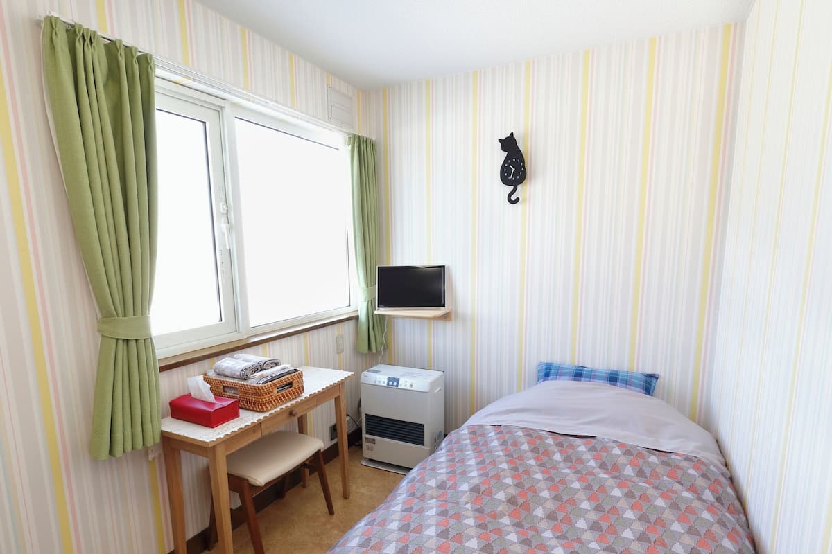 Ein Zimmer mit einem Bett, einem Schreibtisch mit Stuhl, einem Fernseher und einer Wanduhr.