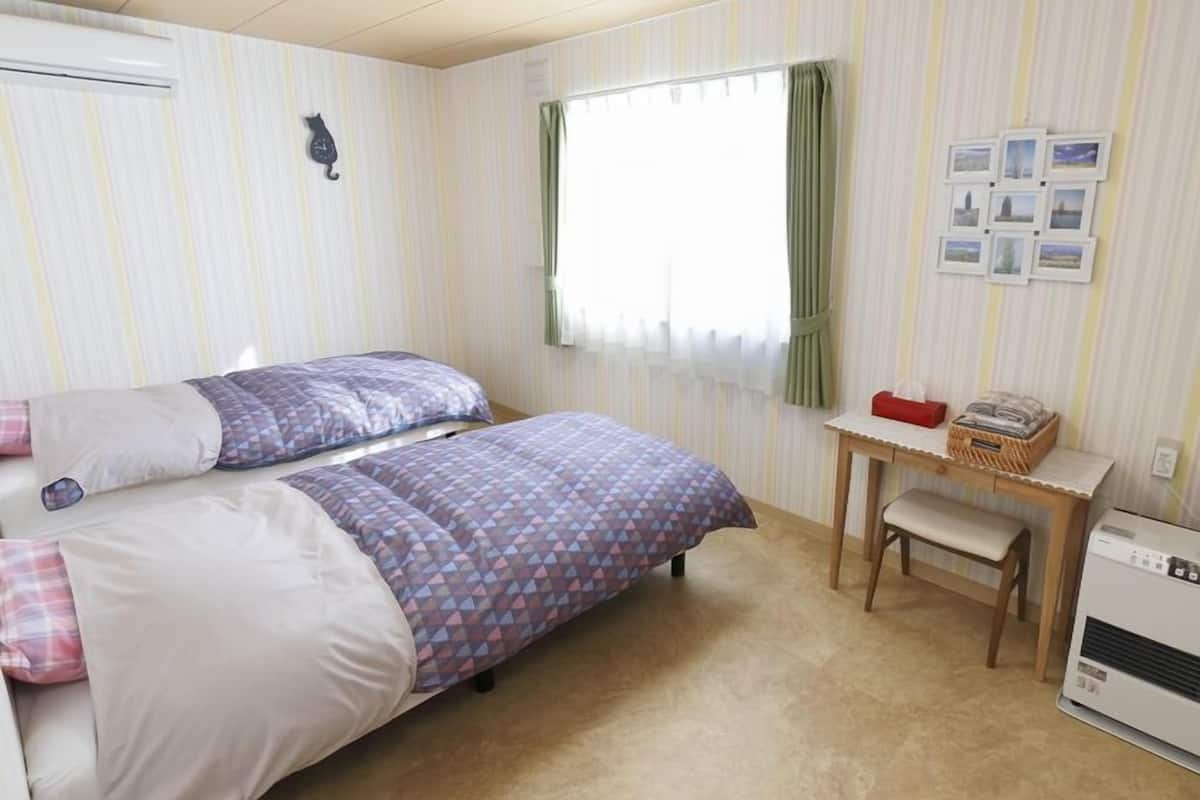Ein Schlafzimmer mit zwei Betten, einem kleinen Tisch, einer Bank, einem Wandheizkörper und einem Fenster mit Vorhängen.