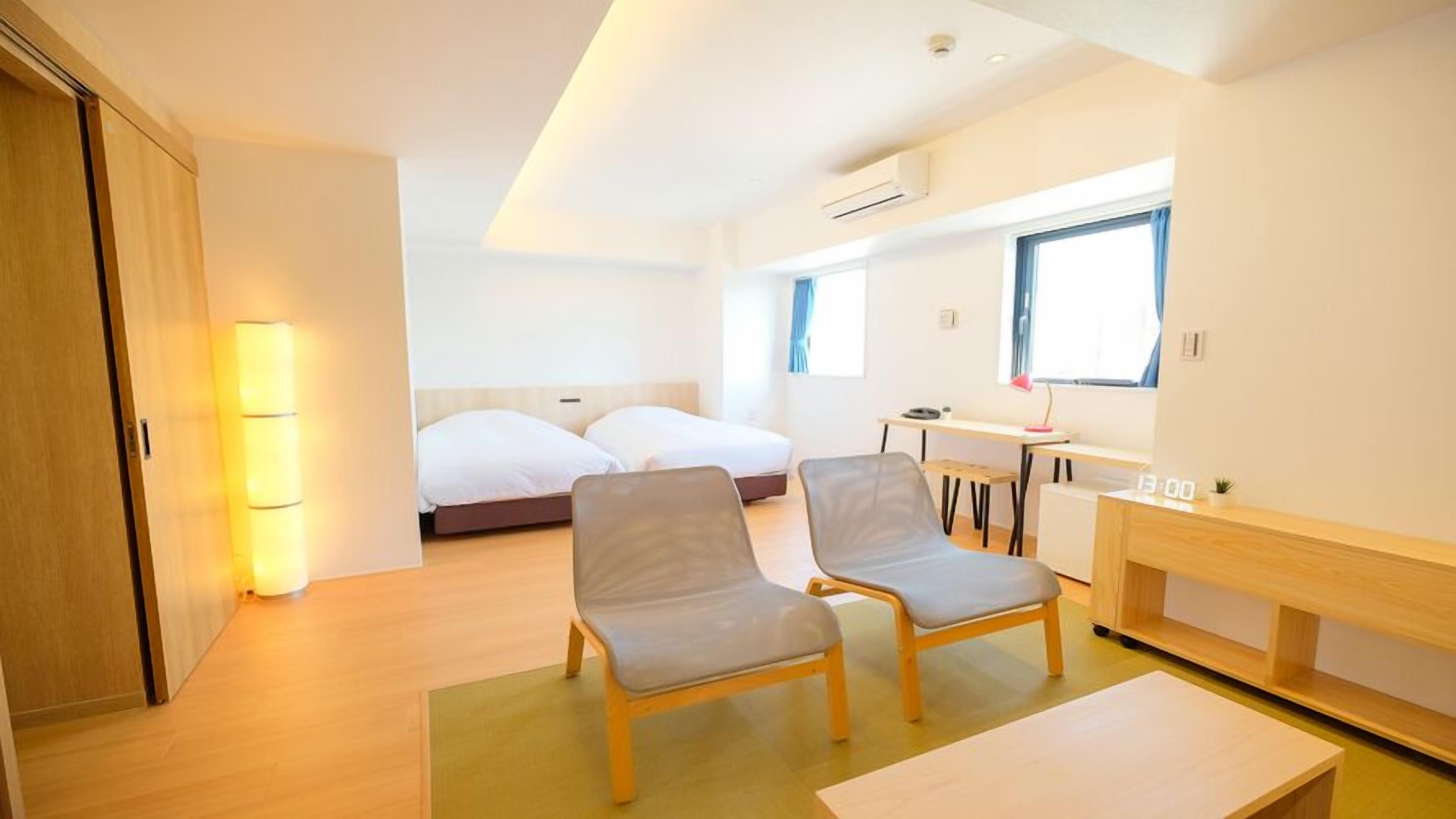 A modern hotel room with a bed, two chairs, a desk, and a small table.