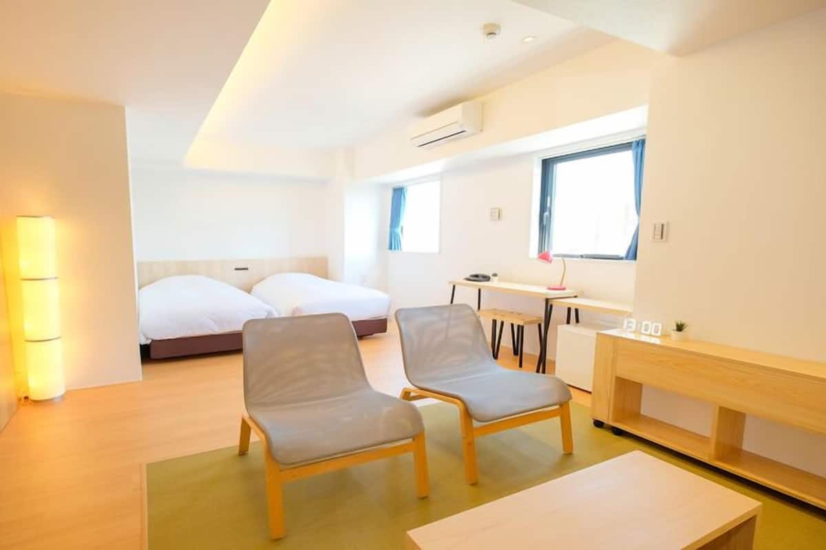 Una habitación de hotel moderna con cama, dos sillones, escritorio y una mesita.