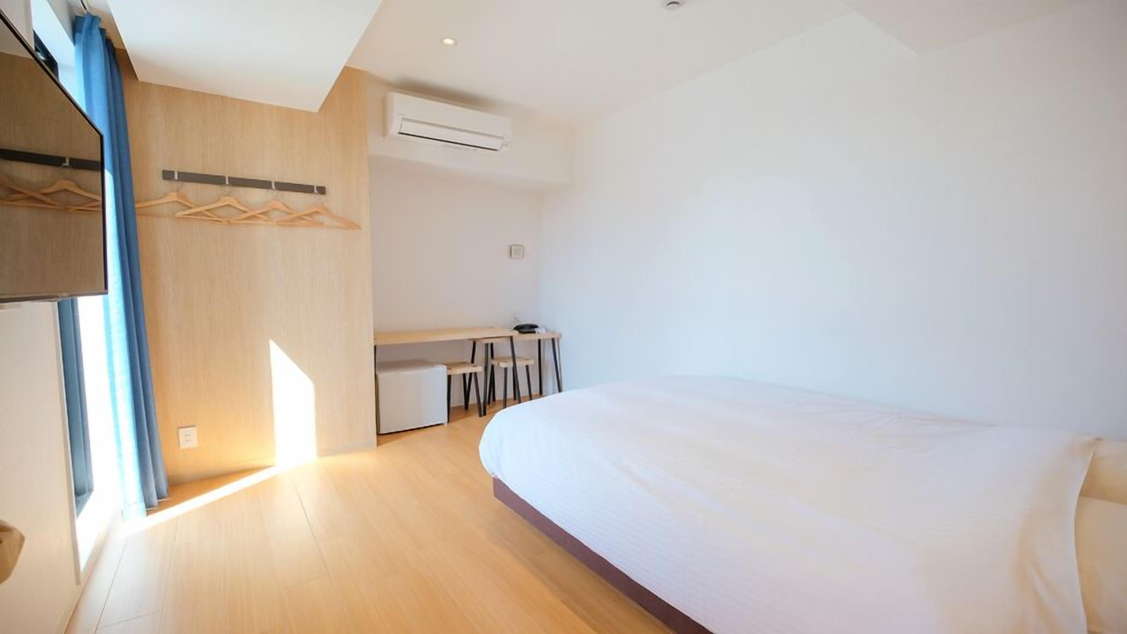 A modern hotel room with a large bed, a desk, and a wardrobe.