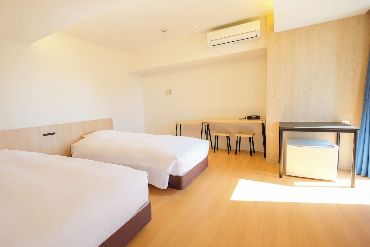 Habitación de hotel con dos camas, un escritorio, una silla y aire acondicionado.