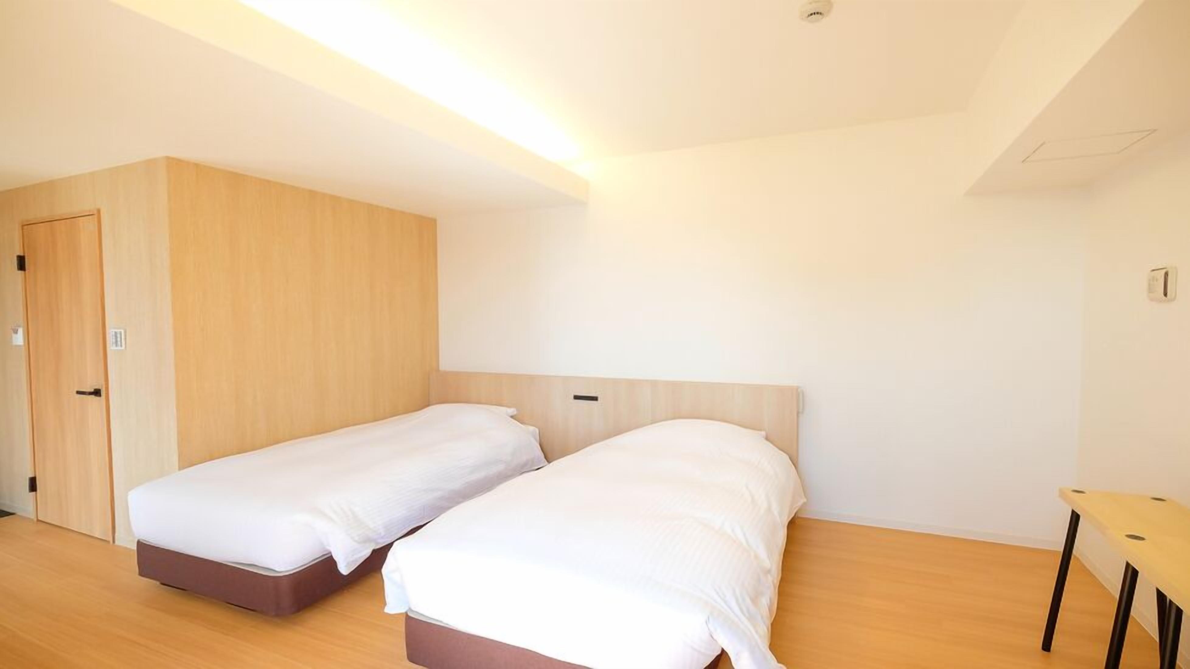 A room with two single beds, a wooden wardrobe, a small table, and a ceiling light.