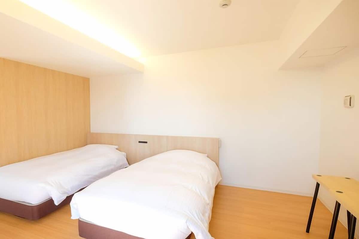 Una habitación con dos camas individuales, un armario de madera, una mesita y una lámpara en el techo.