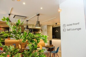 A modern hotel lobby with a self-lounge area, a reception desk, and a staircase.
