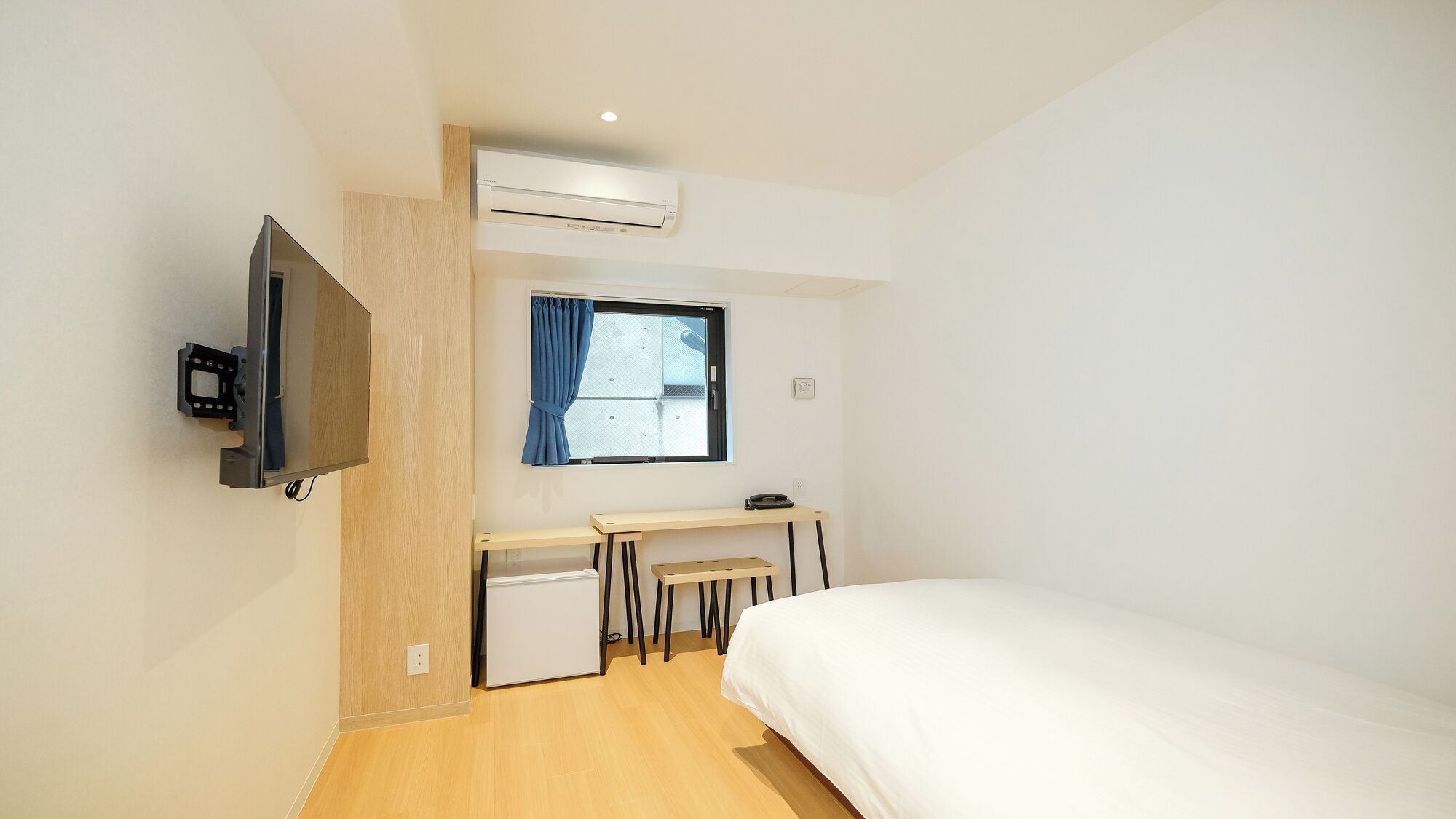 A hotel room with a bed, a desk with a chair, a television, and an air conditioning unit.