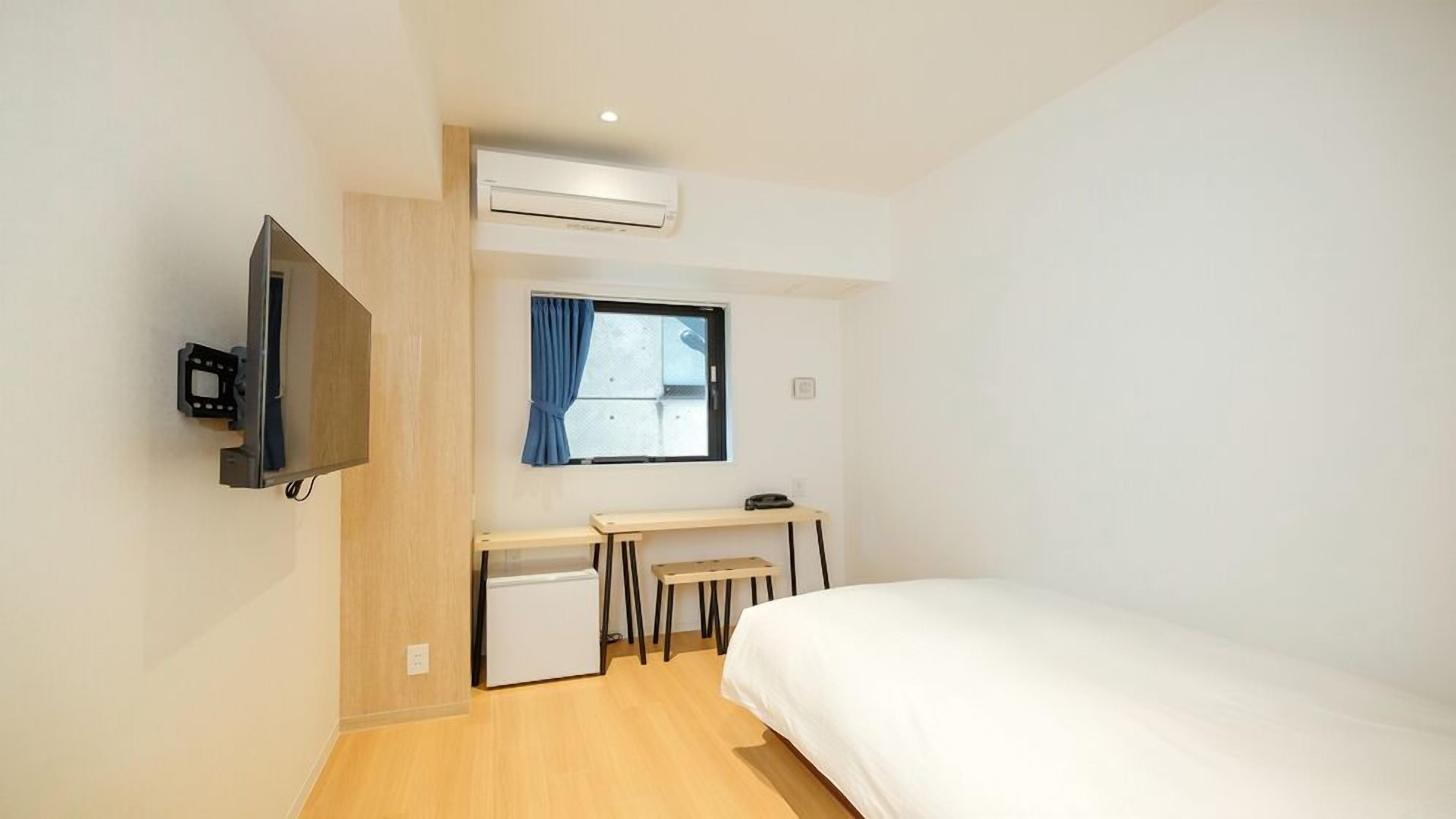 A compact hotel room with a bed, a desk, a television, and an air conditioning unit.
