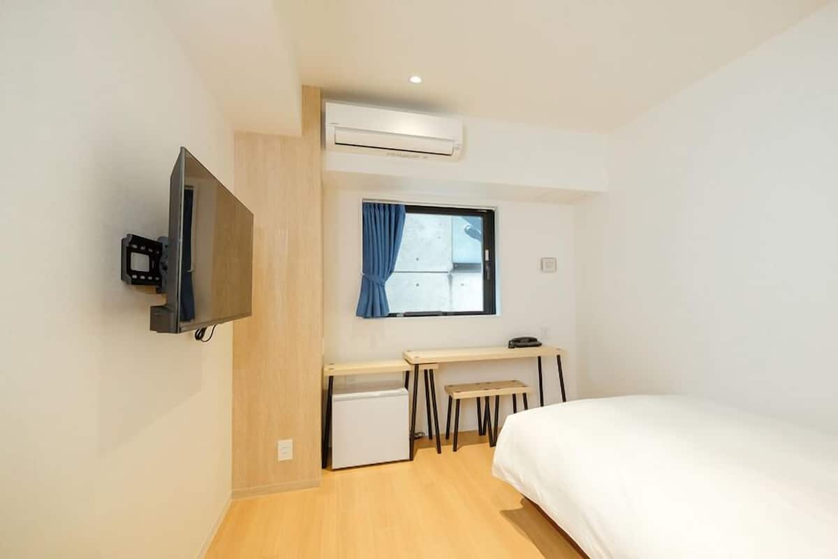 Habitación de hotel compacta con cama, escritorio, televisor y aire acondicionado.