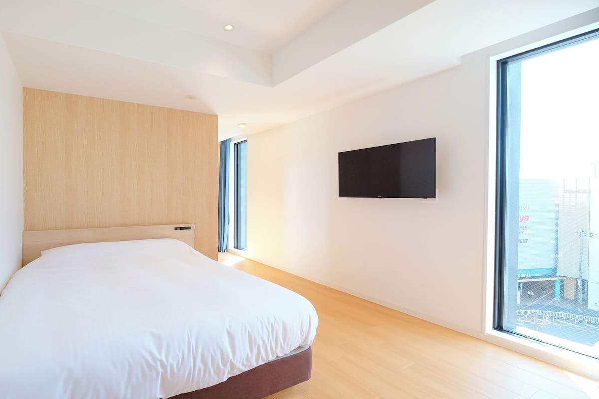 Un dormitorio moderno con una cama grande, un televisor montado y un ventanal amplio.