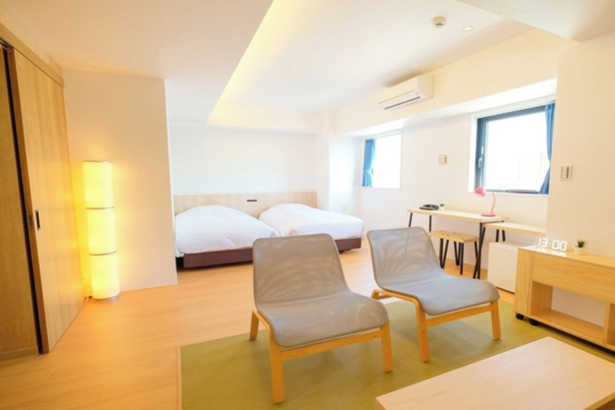 A modern hotel room with a bed, two chairs, a desk, and a small table.