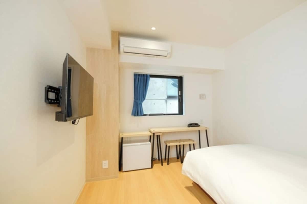 Una habitación pequeña y limpia con cama, escritorio, televisor y aire acondicionado.