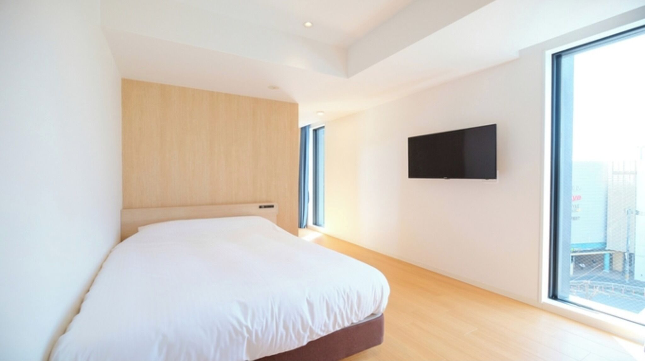 A modern bedroom with a large bed, a mounted TV, and a large window.