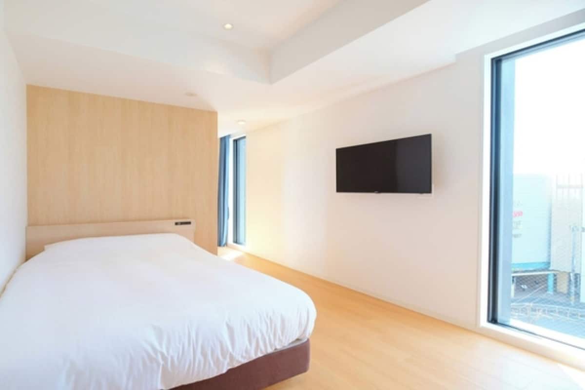 Un dormitorio moderno con una cama grande, un televisor montado y un ventanal amplio.