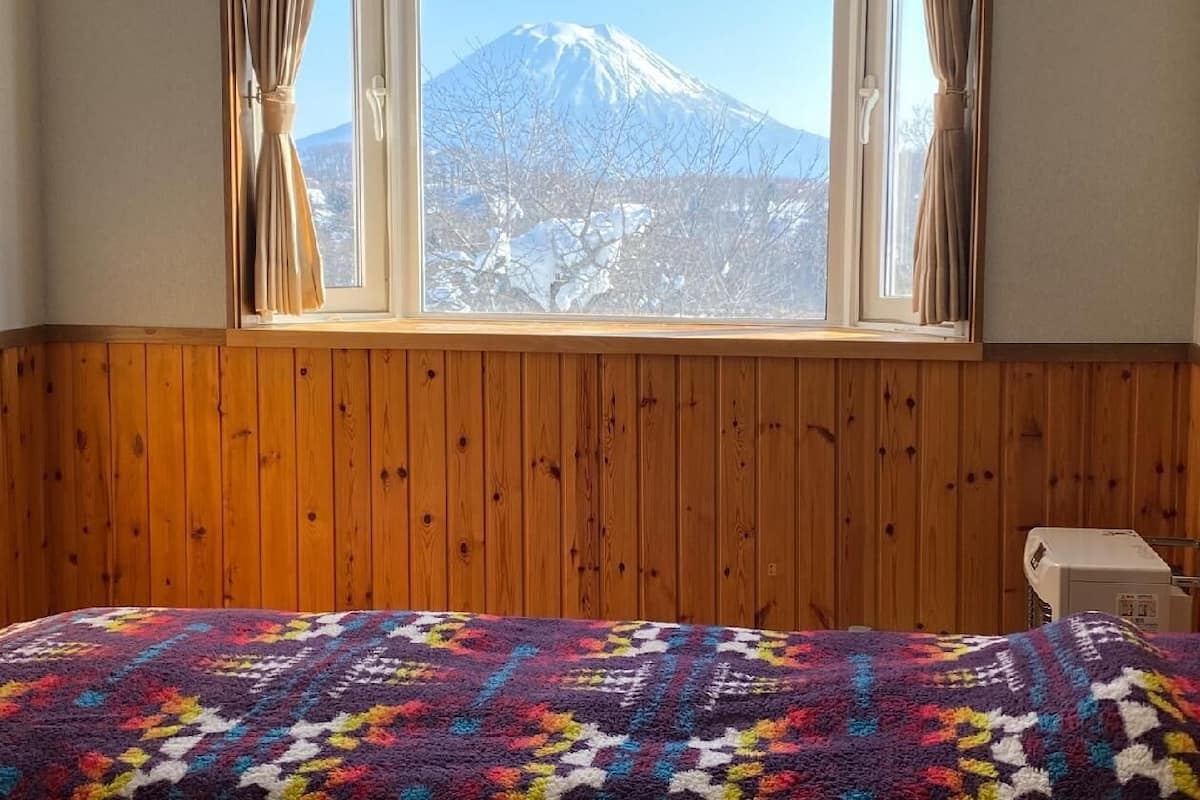 A room with a wooden paneled wall, a bed with a colorful blanket, and a window with curtains.