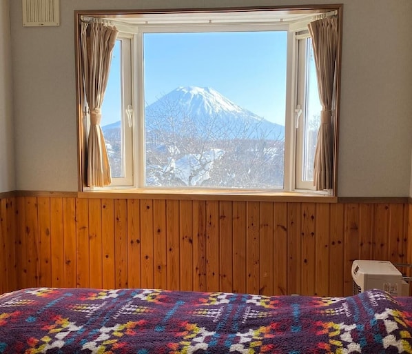 A room with a wooden paneled wall, a bed with a colorful blanket, and a window with curtains.