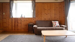 A room with wooden panel walls, a sofa, a small table, and a window with curtains. - Fureai no Sato Hinode (Rankoshi)