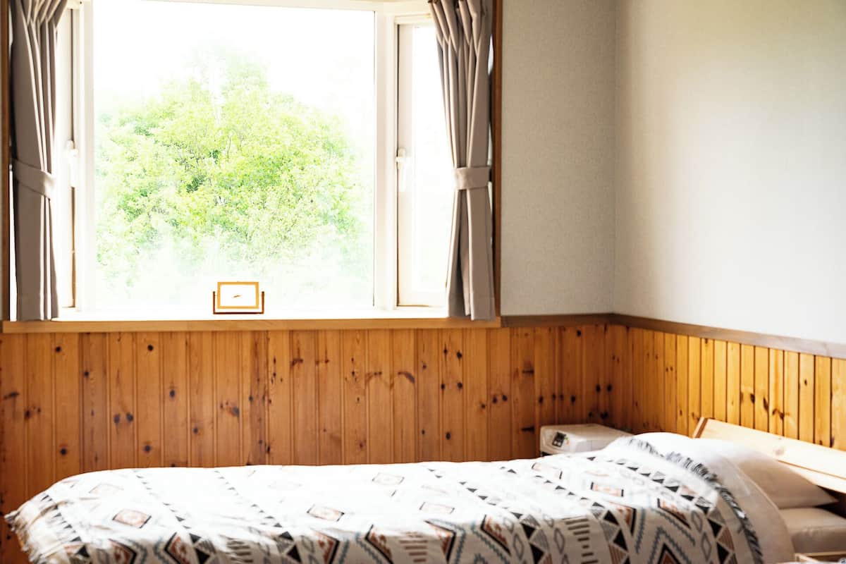 A room with a wooden paneled wall, a bed with patterned bedding, and a window with curtains.