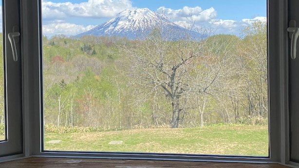 A room with a large window offering a view of a snow-capped mountain and a forested area. - Fureai no Sato Hinode (Rankoshi)
