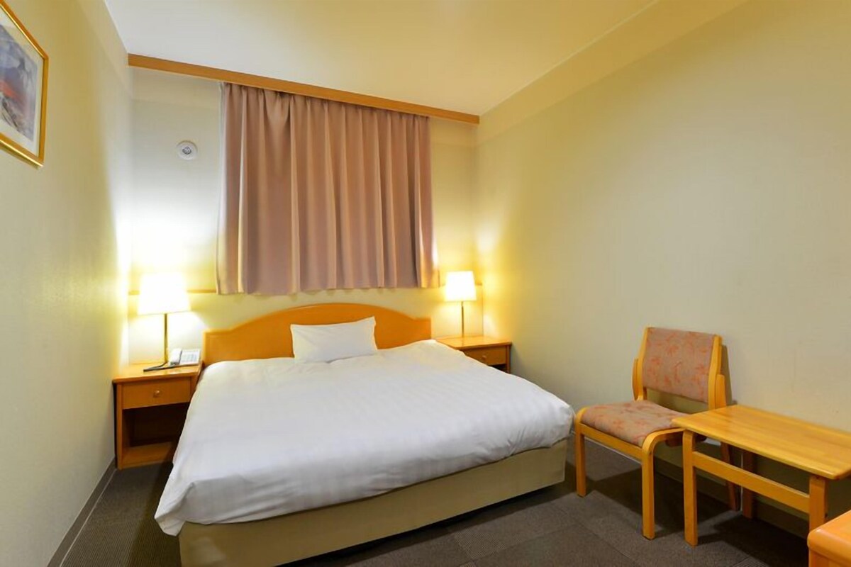 Ein Hotelzimmer mit Bett, Nachttischlampen, einem Sessel und einem kleinen Tisch.
