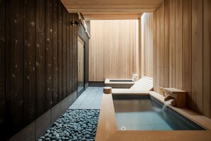 A modern spa with a wooden interior, a hot tub, and a pebble-lined walkway.