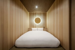 A minimalist bedroom with a large bed, wooden paneling, and a circular light fixture.