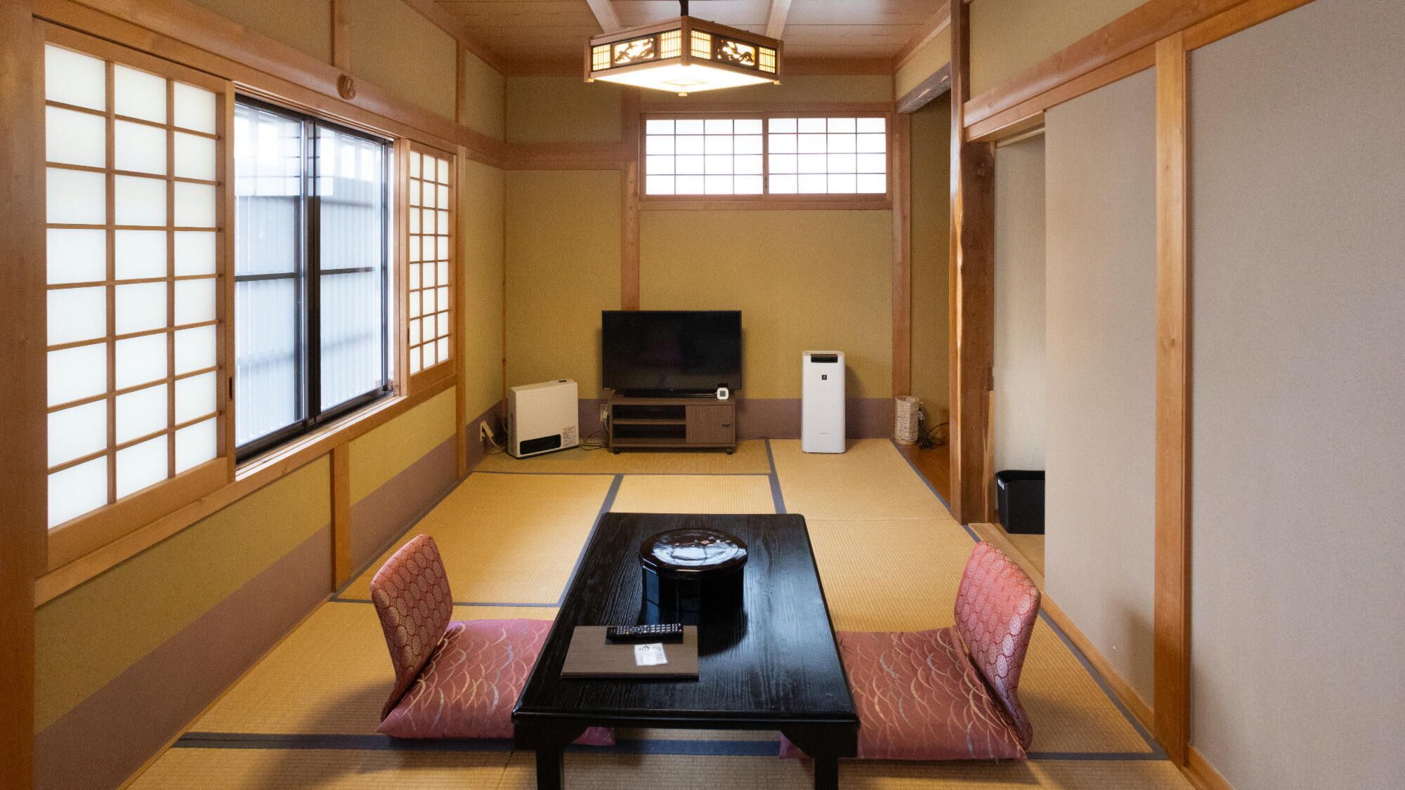 Um quarto japonês tradicional com tatame, uma mesa baixa com almofadas, uma televisão e um aquecedor.