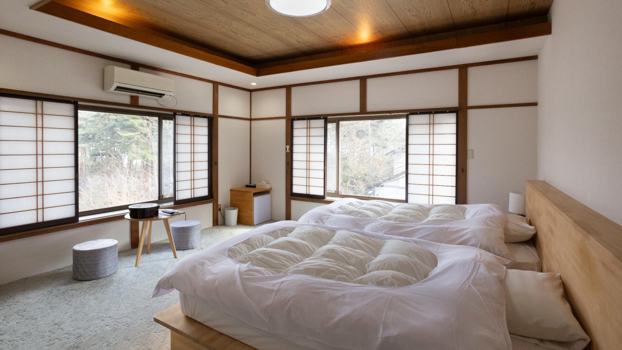 Quarto tradicional em estilo japonês, com piso de tatame, futon, pequena escrivaninha de madeira e janela com portas shoji.